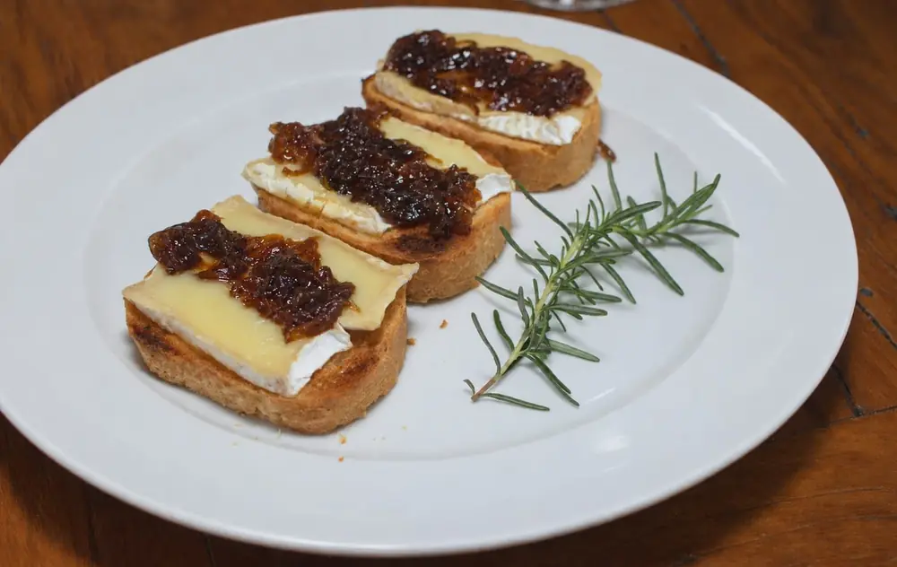 Torradas com queijo brie e cebola caramelizada, decoradas com alecrim